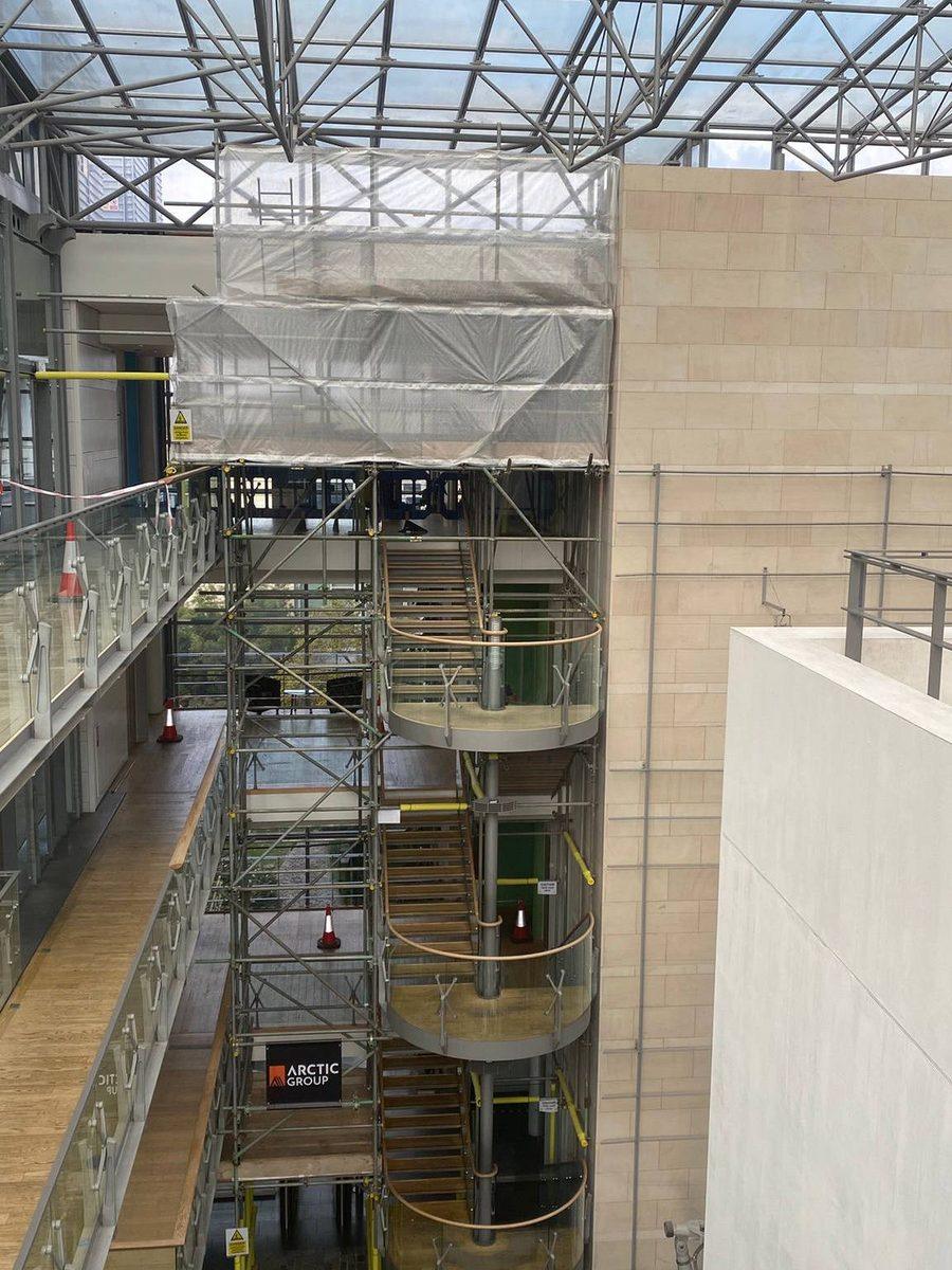 Stair tower scaffold rising through a glazed office atrium