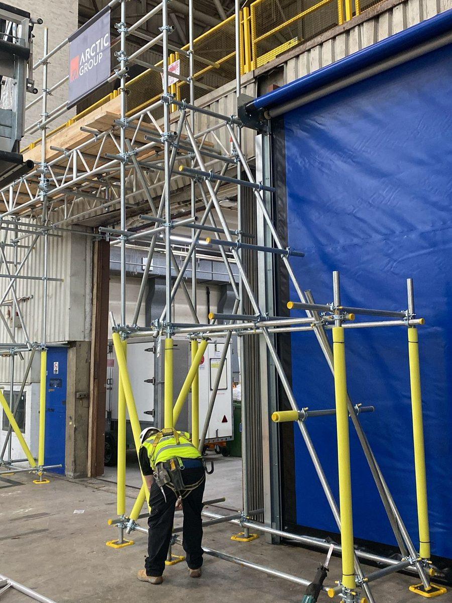 Arctic Scaffolding operative building a tower beside a hangar door