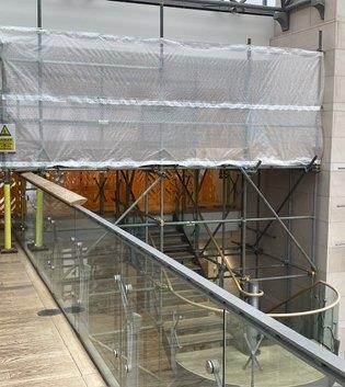 Yellow-padded gantry keeping a garden path open beside a flint wall
